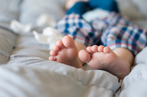 Child lying in bed with tissues around him.  Focus on foot and toes.