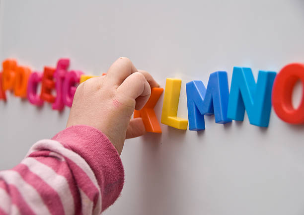 Learning the Alphabet A Pre-School girl arranges multicoloured magnetic letters into the alphabet on a white board. kids using smart board stock pictures, royalty-free photos & images