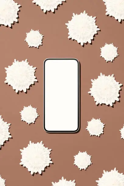 Photo of Smartphone mockup with origami paper snowflakes on brown background.