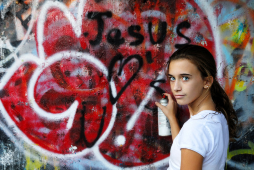 A young teen tags a wall with Jesus Loves U