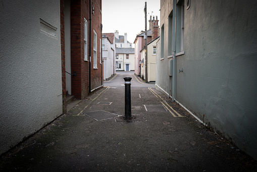 Shallow focus of an erected street bollard located down a narrow side street in the Suffolk seaside town of Aldeburgh. The bollard presents vehicles from taking shortcuts to the nearby beach.