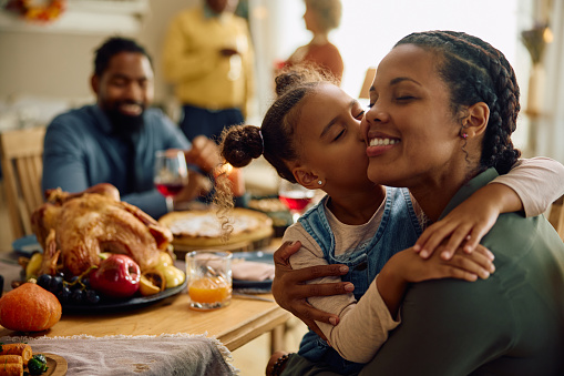 Affectionate African American girl kissing her mother while having family dinner on Thanksgiving.