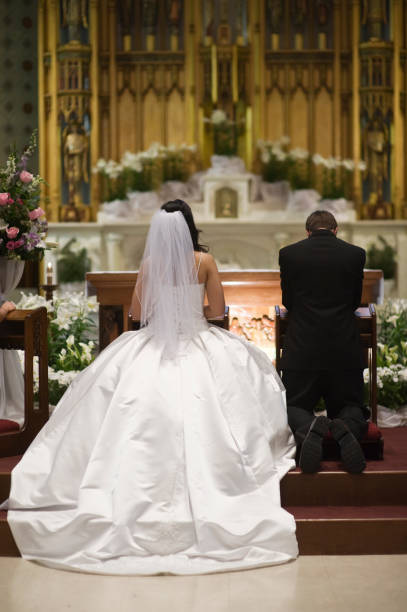 Rear view of a bride and groom kneeling at altar at wedding stock photo