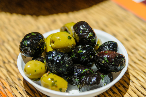 A bowl of green and black olives, sprinkled with herbs