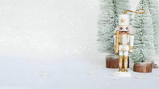 Christmas Nutcracker toy figurine ornament in white. Decoration for New Year.  Nutcracker on the white sparkling background with conifers. Advent concept with bokeh lights.