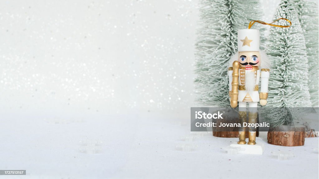 Christmas Nutcracker toy figurine ornament in white. Decoration for New Year.  Nutcracker on the white sparkling background with conifers. Advent concept with bokeh lights. Christmas Stock Photo
