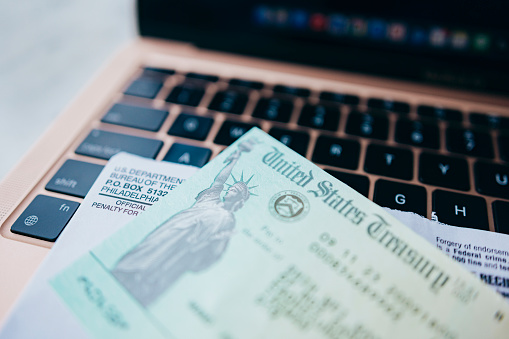 Close-up of a tax refund check on a table, with a laptop in the background.
