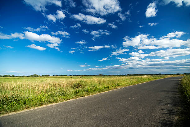 A landscape portrait of a road, green grass and blue sky stock photo