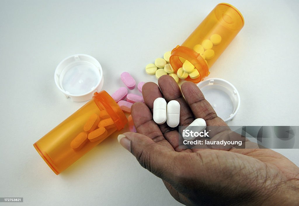 African-American Hand Holding Medication An African-American hand holds three pills. Background has two pills bottles and two other types of medicine. African Ethnicity Stock Photo