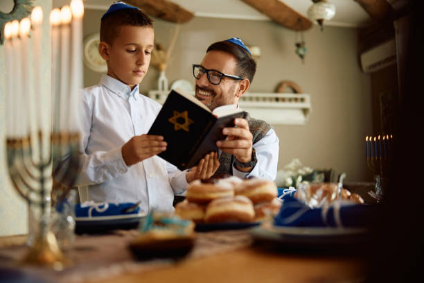 Happy father and son reading Hebrew bible during Hanukkah at home. Jewish boy and his father reading Tanakh while celebrating Hanukkah at home. orthodox jew boy stock pictures, royalty-free photos & images