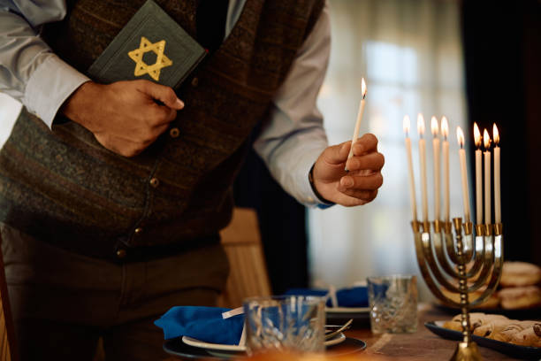 istock Close up man holding Hebrew bible while lighting the menorah. 1727539900