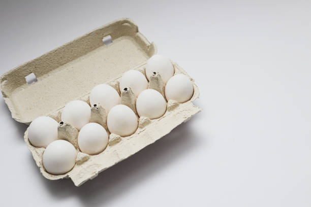 istock Ten white eggs in a carton package. Cardboard egg box on orange background 1727548428