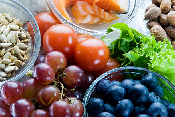Close up of word health made of red and green cheery tomatoes on black cutting board surrounded by variety of fresh vegetables on wooden table