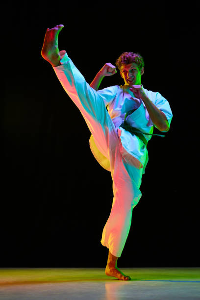 istock Professional combat sport. Young guy, karate athlete in motion, practicing leg kicks over black studio background in neon lights 1727574658