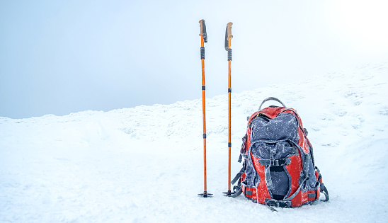 Trekking sticks and backpack standing on snow under clear winter sky
