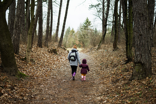 Back of mom with backpack and daughter walking along the forest after rain together.