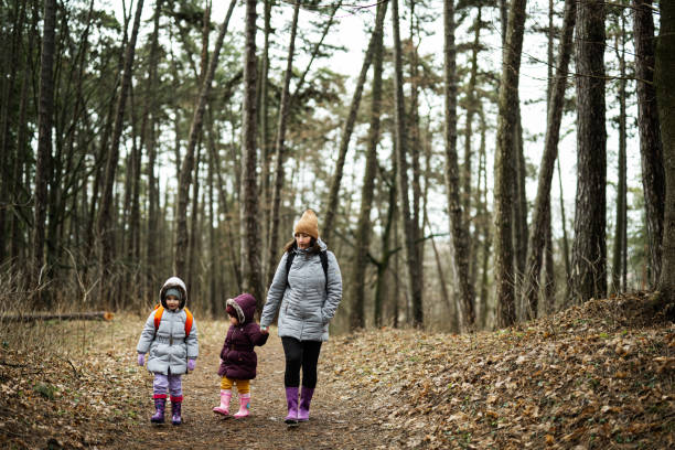 istock Mother and two daughters with backpacks walking along the forest road together. 1727583865