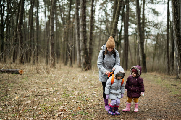istock Mother and two daughters with backpacks walking along the forest road together. 1727583906