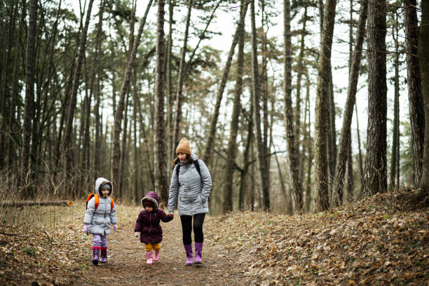istock Mother and two daughters with backpacks walking along the forest road together. 1727585539