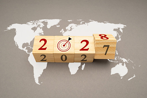 Business planning and countdown to 2028. Flipping 2027 to 2028 on wooden cubes over the world map background