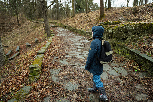 Back of boy with backpack walking along the forest stone road after rain.