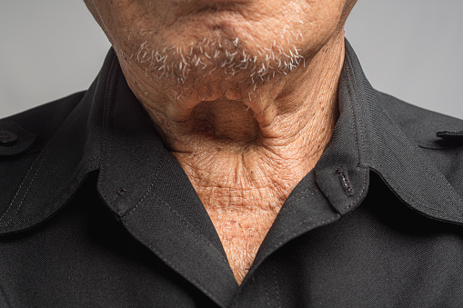 Close-up of wrinkled neck a senior man while standing on a gray background. Body skin part. Aged people and healthcare concept