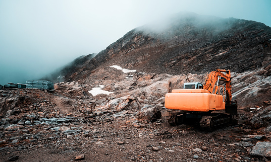 Bulldozer cutting surface of Alps covered with clouds