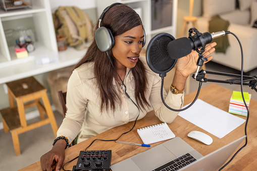 Photo of young women recording podcast with microphone and laptop in recording studio.