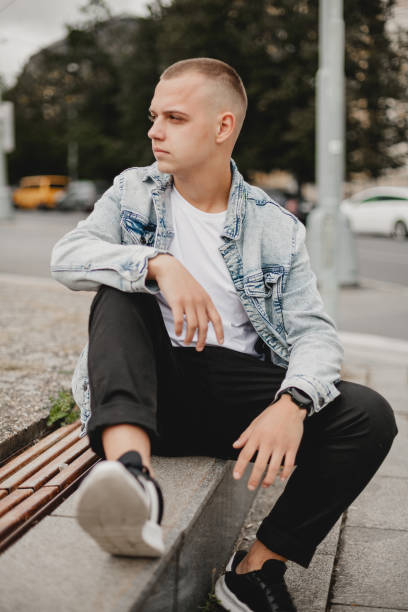 urban contemplation. young man in denim jacket deep in thought. city musing. brooding young guy in stylish denim jacket. thoughtful urbanite. young man reflecting in his denim jacket - bolero jacket imagens e fotografias de stock