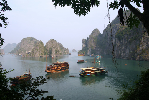 Luxury tour boats sit at anchor in Halong Bay in front of towering limestone karst rock formations as seen from Surprise Cave (Song Sot Grotto) used as a base for the Viet Cong during the Vietnam War.