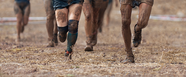 Group of participants in an obstacle course race running. They run very muddy. Concept of hardness and effort