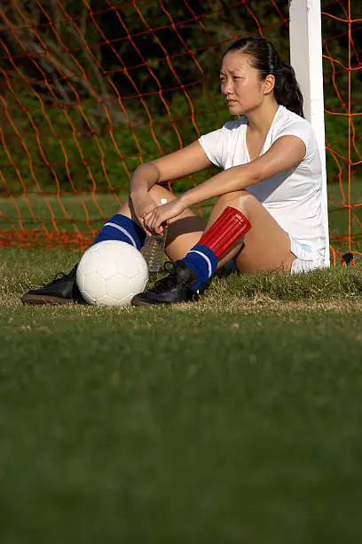 Photo of young female soccer player resting against goal post.