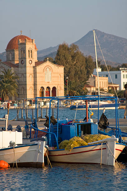 Fishing boats in the harbor on the island of Aegina in Greece.  In the distance is a large church