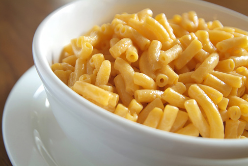 Close up image of delicious and creamy macaroni and cheese in a white bowl sitting on a kitchen table.