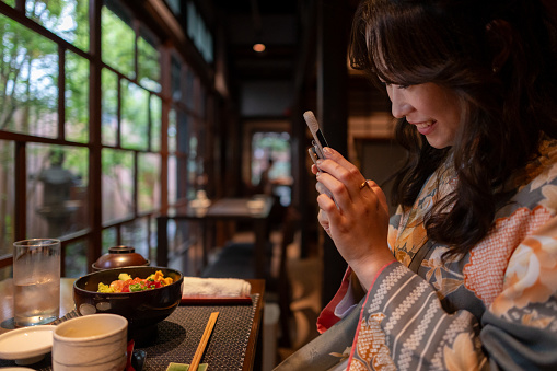 Solo trip woman in Kimono / Hakama taking photos of lunch in traditional Japanese restaurant