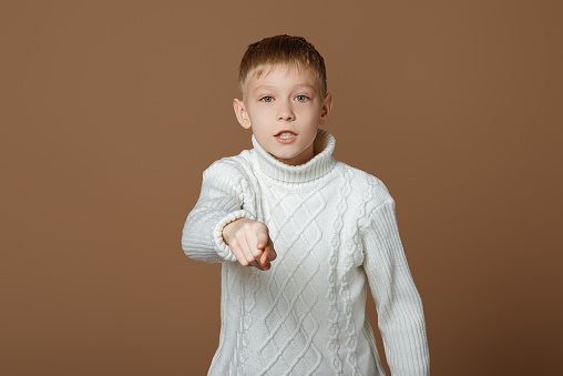 Hey you! Portrait of emotional teen boy pointing finger to camera, looking with suspicion and accusing, choosing guilty, beige studio background