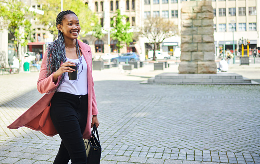 A young black woman happy smiling walking in the city with her cup coffee