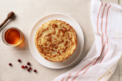 Crepes, thin pancakes with honey on a white plate. Marble background. Top view.