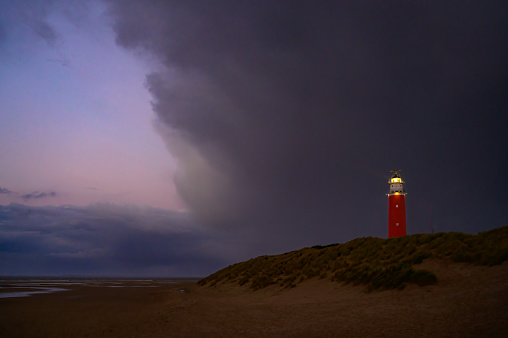 Lighthouse at the Wadden island Texel in the dunes during a calm autumn evening with dramatic clouds in the sky on the North Sea beach. The Eierland lighthouse is located at the North point of the island.