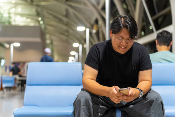 istock Asian man using mobile phone at airport terminal. 1727689855