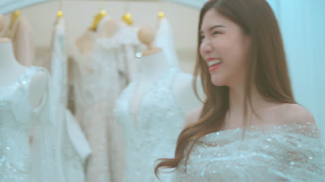 Young Asian bride trying on wedding dresses in wedding studio.