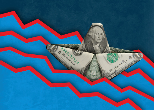A digital composite of a dollar bill paper boat sinking amidst falling graph lines.