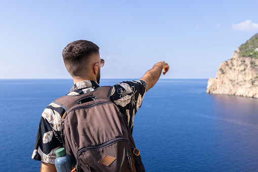 Photo from behind of a caucasian man with short hair who is looking at the view and pointing with his arm.