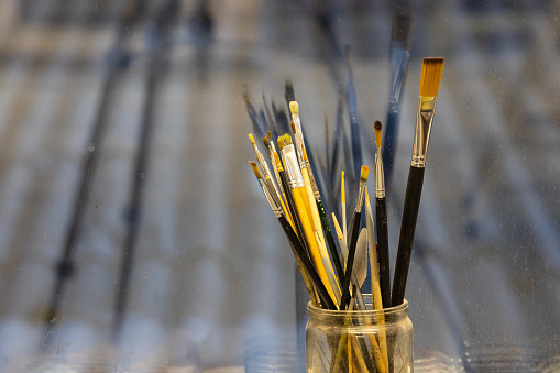 Set of used artistic paint brushes in glass jar against dirty gray background