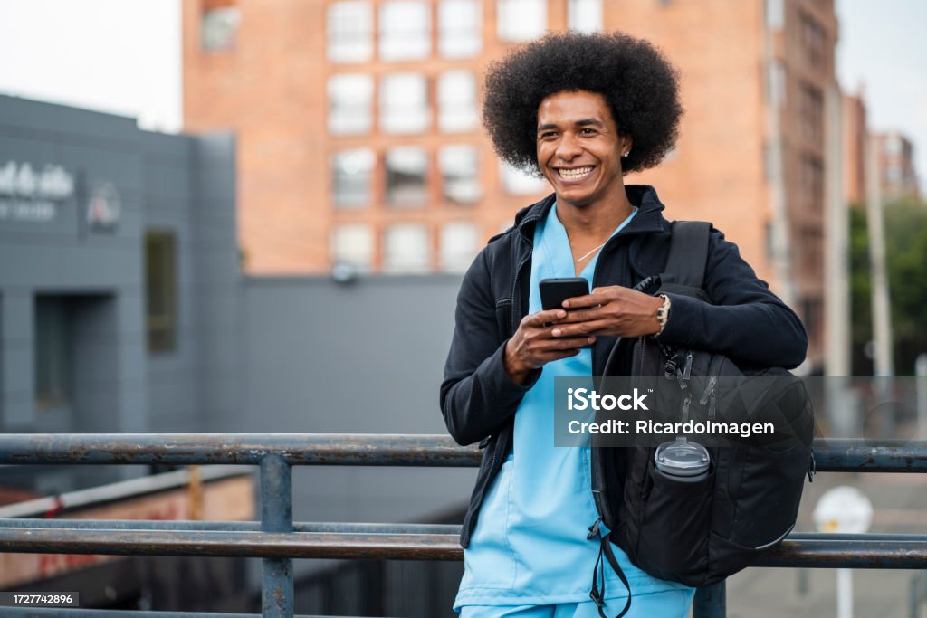 Nurse is using his phone on the streets of the city Nurse of Latino ethnicity between 25-35 years old is using his phone on the streets of the city Nurse Stock Photo
