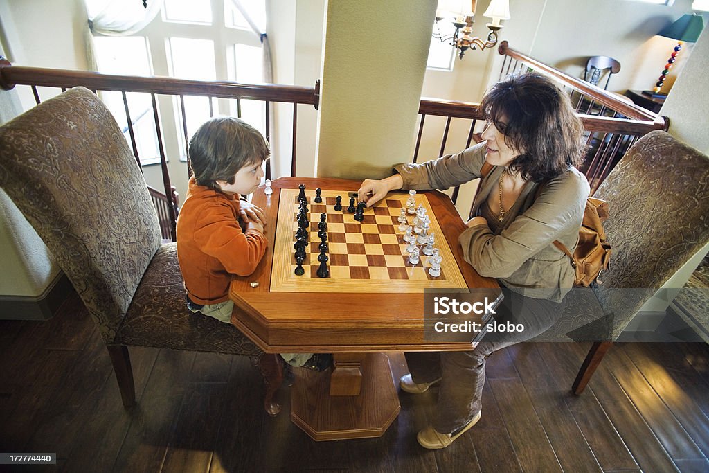 Madre e figlio giocando a scacchi insieme su una scacchiera marrone - Foto stock royalty-free di Figlio maschio