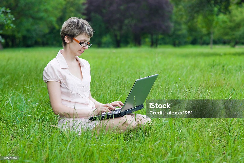 Chica con ordenador portátil s'encuentra en park on green grass - Foto de stock de Adolescencia libre de derechos