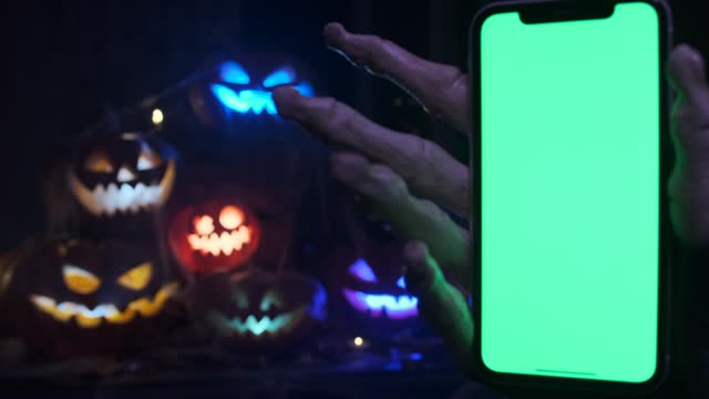 Creepy hand with phone chromakey screen zooms in and out against backdrop of creepy jack-o'-lanterns