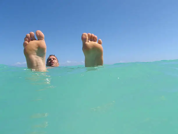 Two large feet jut out of tropical blue waters above the head of their owner