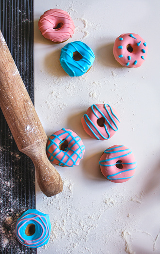 Homemade multi color glazed donuts on table and rolling pin beside